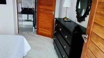 Una camera da letto con un letto, una cassettiera, uno specchio e un bagno parzialmente visibile attraverso una porta aperta.