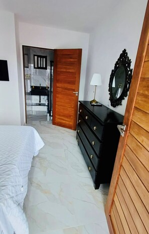 A bedroom with a bed, a dresser, a mirror, and a bathroom visible through an open door. - Residence Pipa Beach (Tibau do Sul)