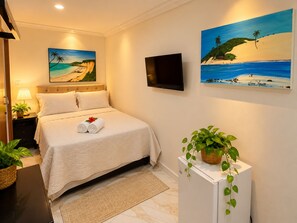 A hotel room with a bed, a flat-screen TV, two paintings of beaches, a small plant, and a nightstand with a lamp. - Residence Pipa Beach (Tibau do Sul)