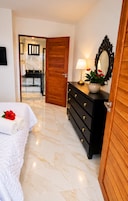 Habitación de hotel con cama, cómoda de madera, espejo y baño visible a través de una puerta abierta.