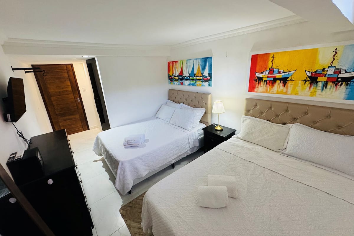 Quarto de hotel com duas camas, televisão de tela plana, escrivaninha e obras de arte nas paredes.