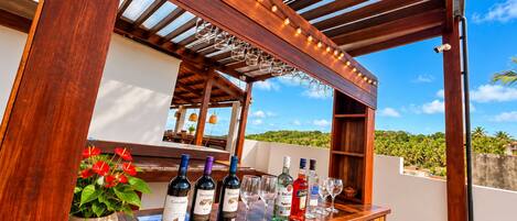 Una barra de madera con botellas y vasos, una planta en maceta y vistas del paisaje.