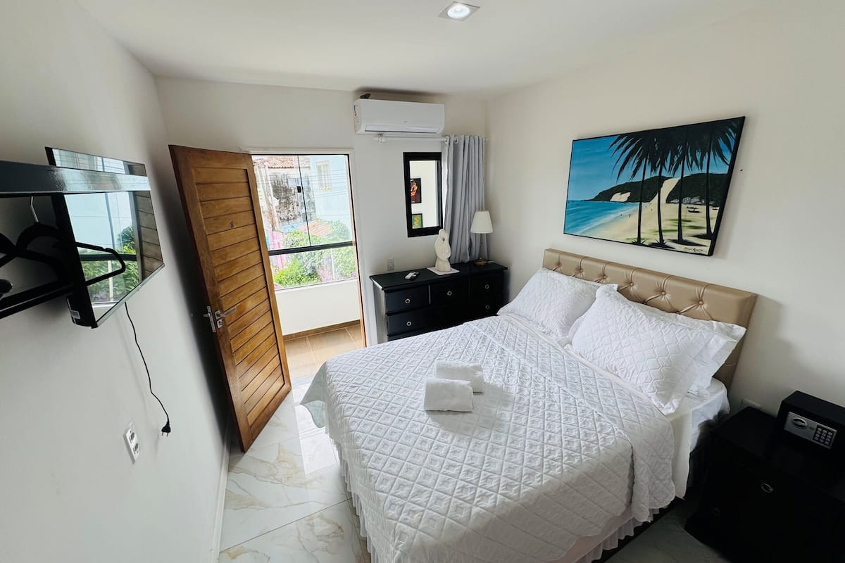 Quarto de hotel com cama, televisão, pintura e varanda.