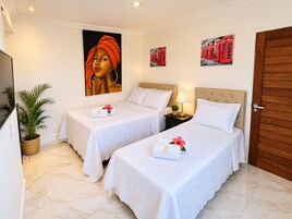 A hotel room with two beds, a painting on the wall, a potted plant, and a wooden door.