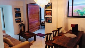 A living room with a sofa, a coffee table, and a dining area with a table and chairs. There are framed pictures on the walls and a wooden door leading to another room. - Residence Pipa Beach (Tibau do Sul)