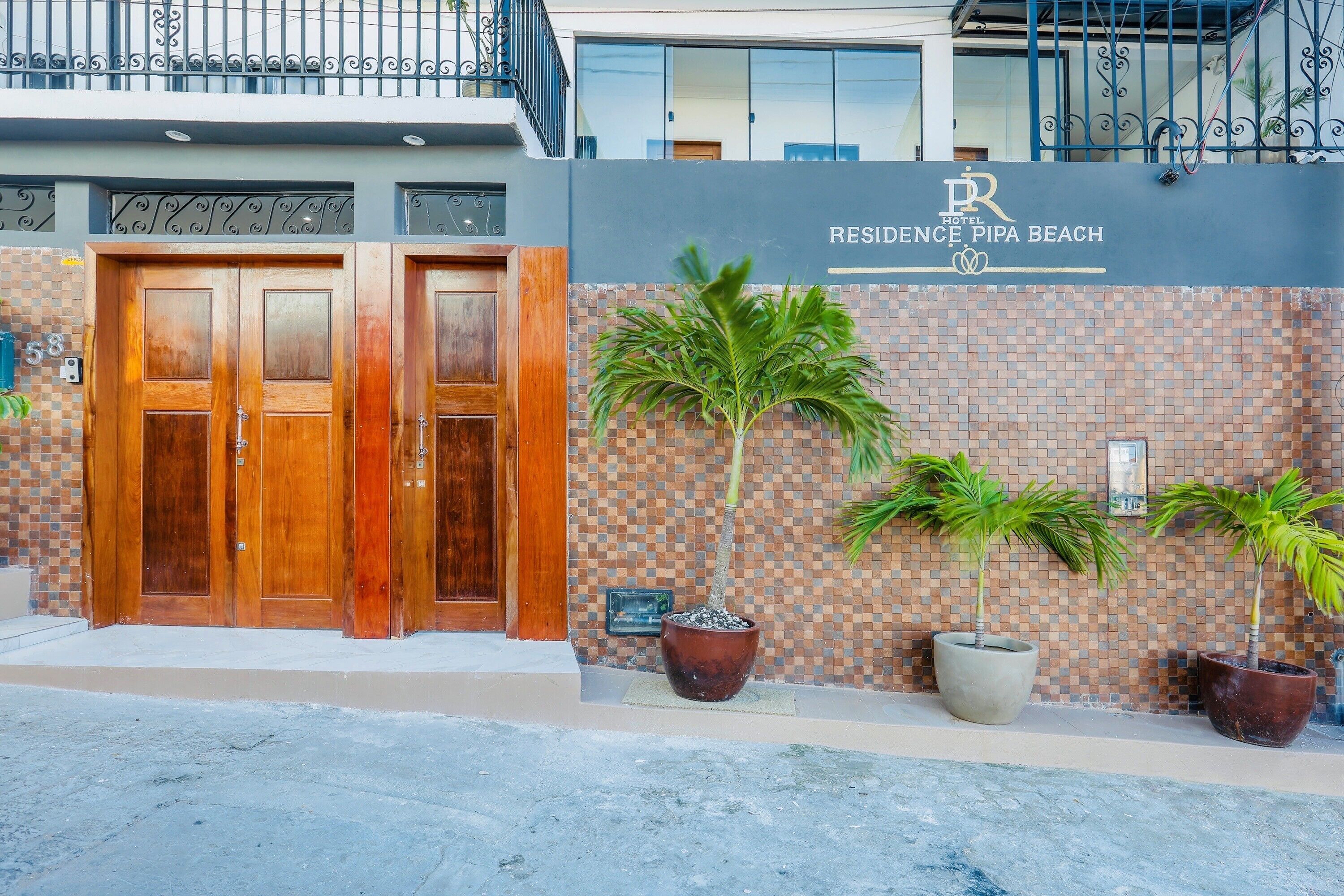 A hotel entrance with double wooden doors, a tiled wall with a mosaic pattern, and potted plants.