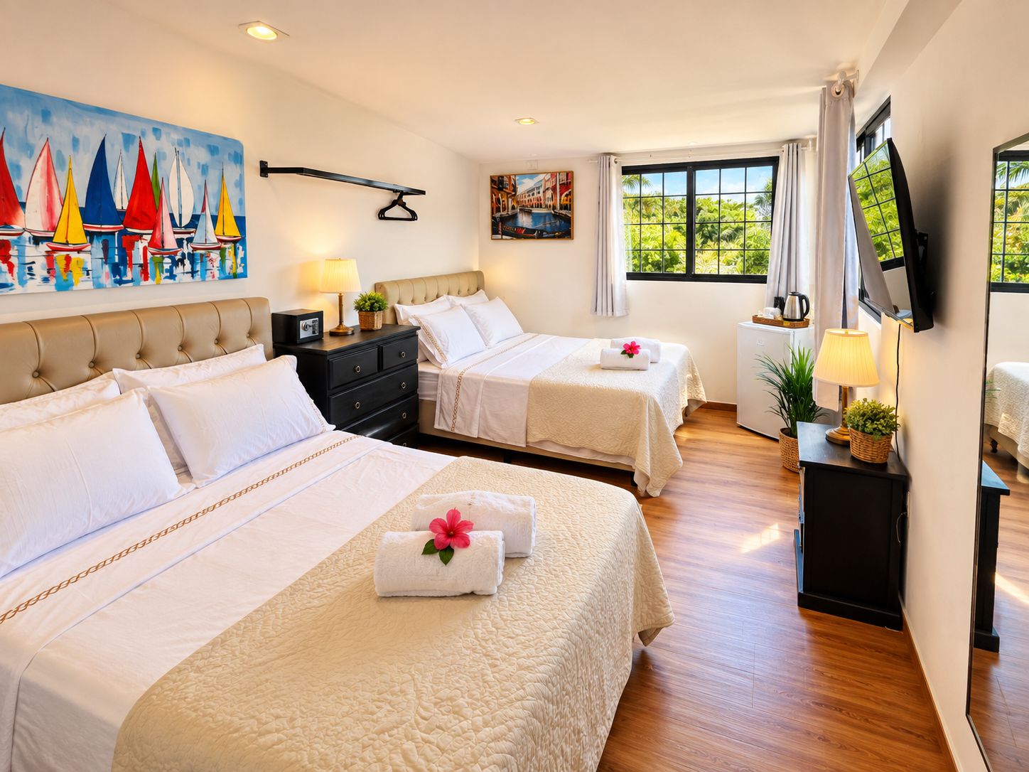 A hotel room with two beds, a TV, a painting of sailboats, and a window with a view of greenery.