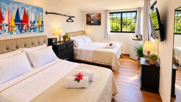 A hotel room with two beds, a TV, a painting of sailboats, and a window with a view of greenery.