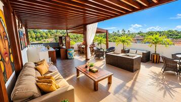 An outdoor patio with a sofa, chairs, a table, and a view of palm trees and buildings.