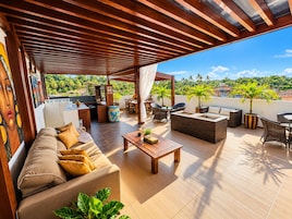 Un patio exterior con un sofá, sillas, una mesa y vistas a palmeras y edificios.