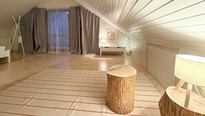 A spacious attic room with a sloped ceiling, a wooden floor, a large window with curtains, a bedside table, and a lamp. - H&H HOME - Cosy Rooftop Apartment with Loggia (Sindelfingen)