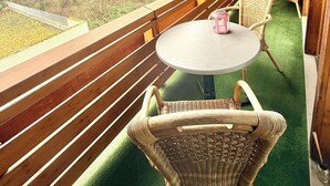 A wooden deck with a round table and wicker chairs, overlooking a green area with trees. - H&H HOME - Cosy Rooftop Apartment with Loggia (Sindelfingen)