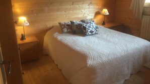 A cozy bedroom with a wooden ceiling, a bed with a white quilt, and two bedside lamps.