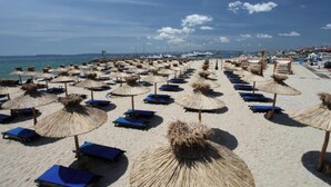 A beach with rows of sun loungers and thatched umbrellas, a clear sky, and a calm sea. - MONASTERY Apart Complex (Sveti Vlas)