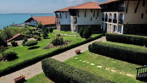 A coastal hotel with a garden pathway, multiple balconies, and a view of the sea. - MONASTERY Apart Complex (Sveti Vlas)