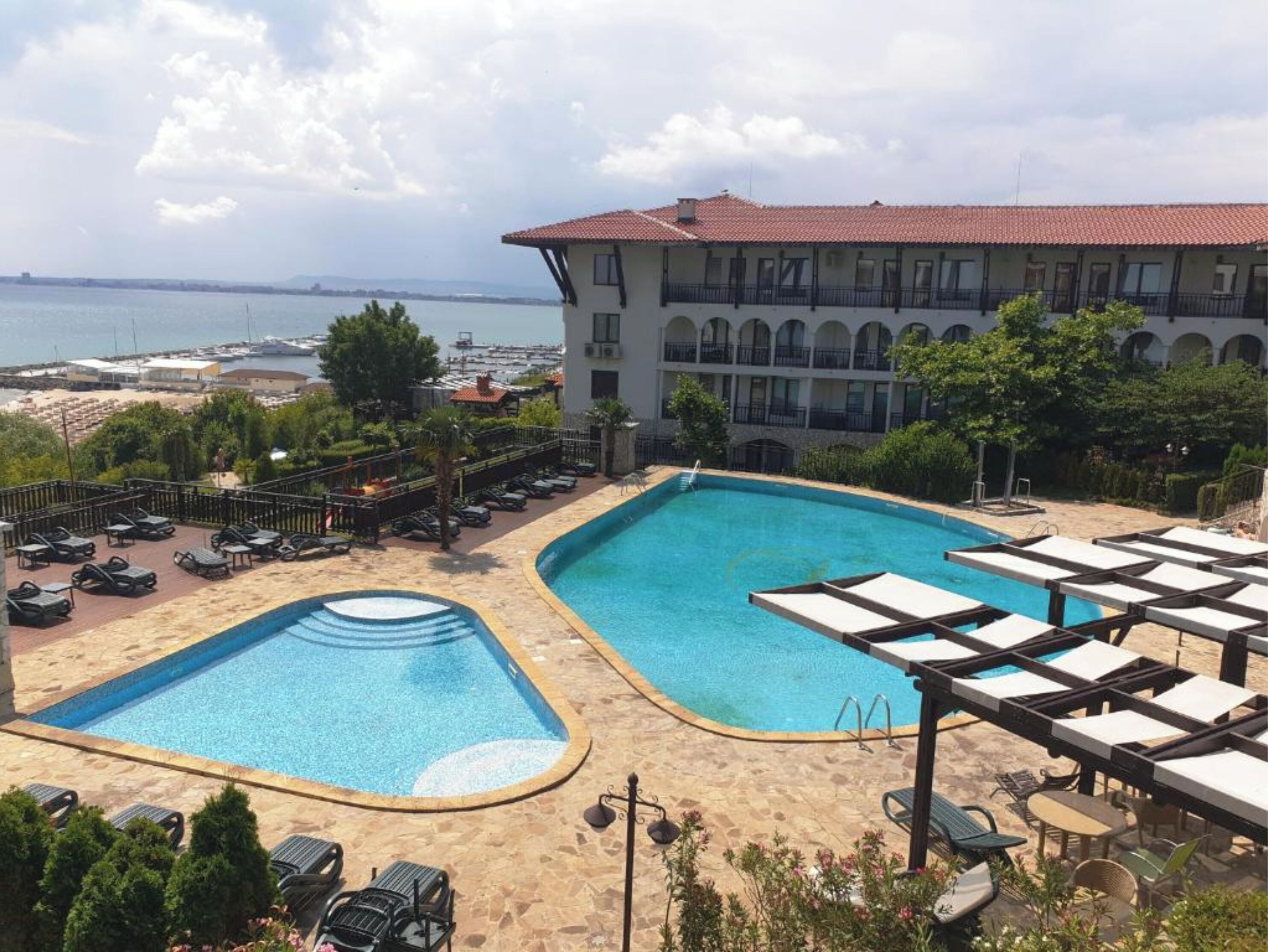 A hotel with a large pool area, including two separate pools and a sun deck with lounge chairs.
