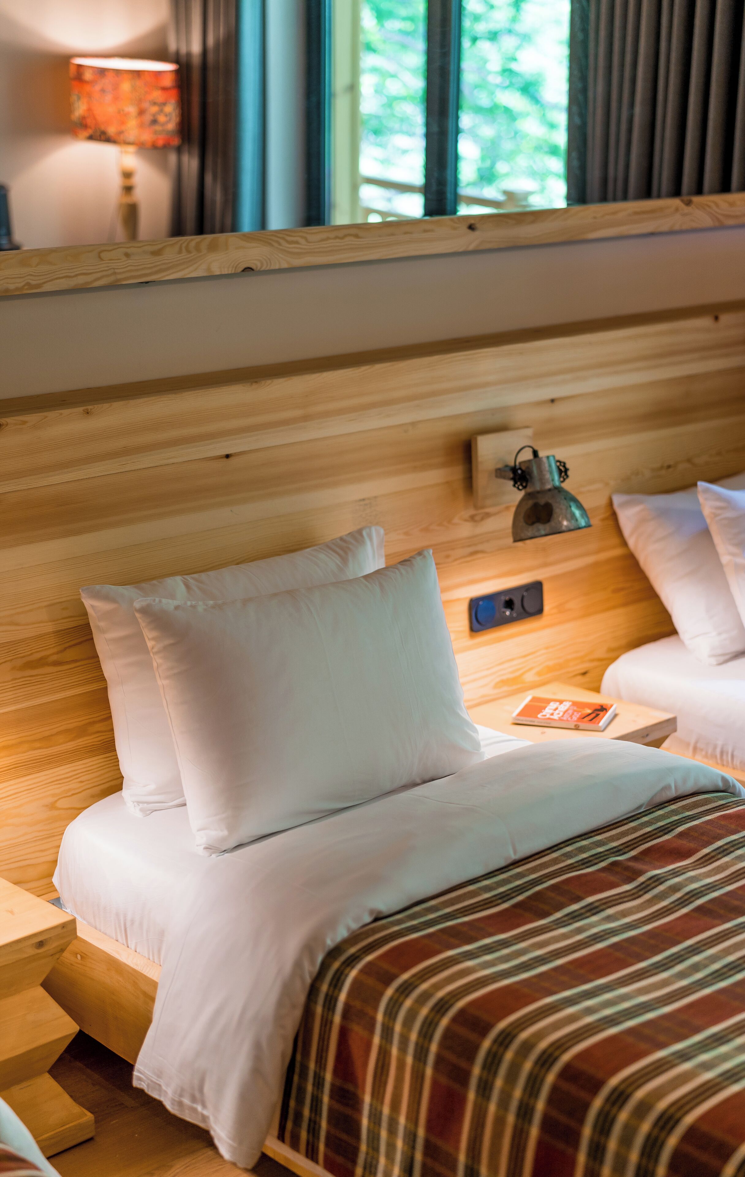 A wooden headboard with a bedside lamp and a book on a nightstand.