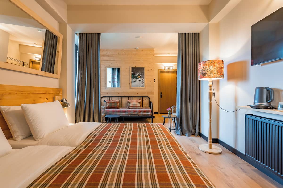 A hotel room with a large bed, a bedside table with a lamp, a small table with a vase, and a view of the hallway.
