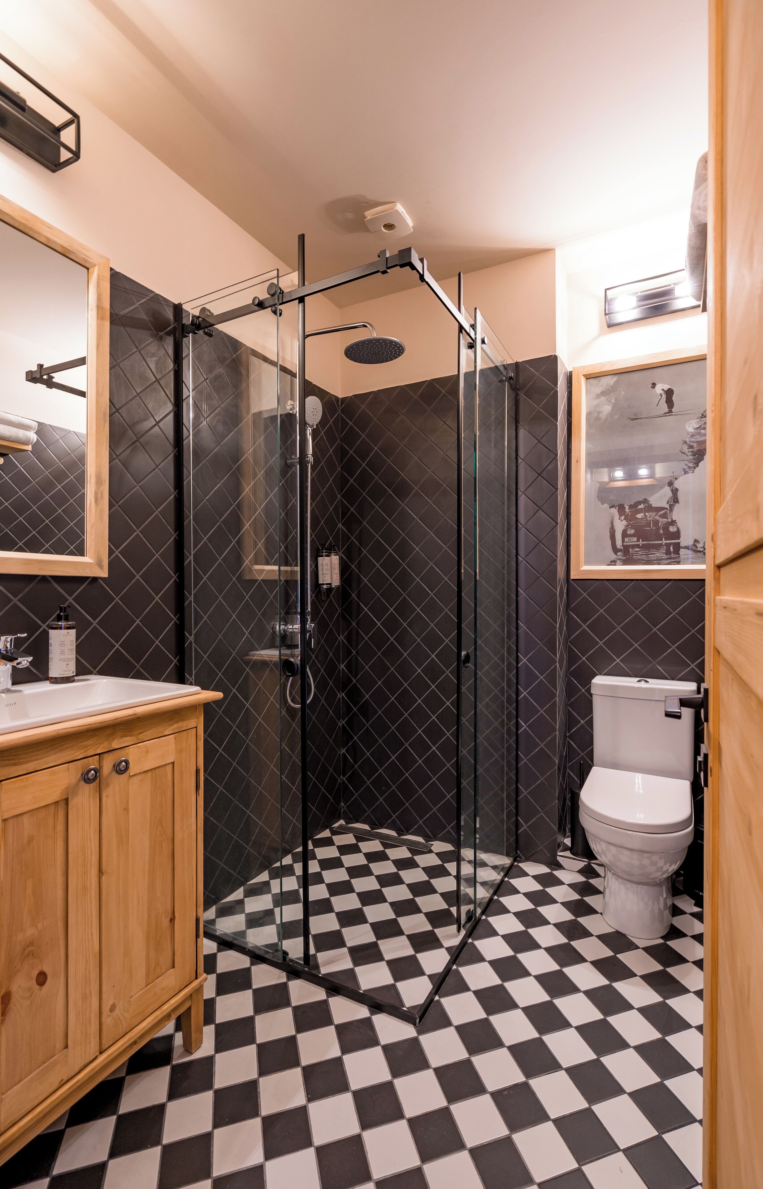 A bathroom with a checkered floor, a glass-enclosed shower, a wooden vanity, and a toilet.