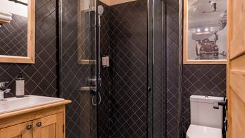 A bathroom with a checkered floor, a glass-enclosed shower, a wooden vanity, and a toilet.