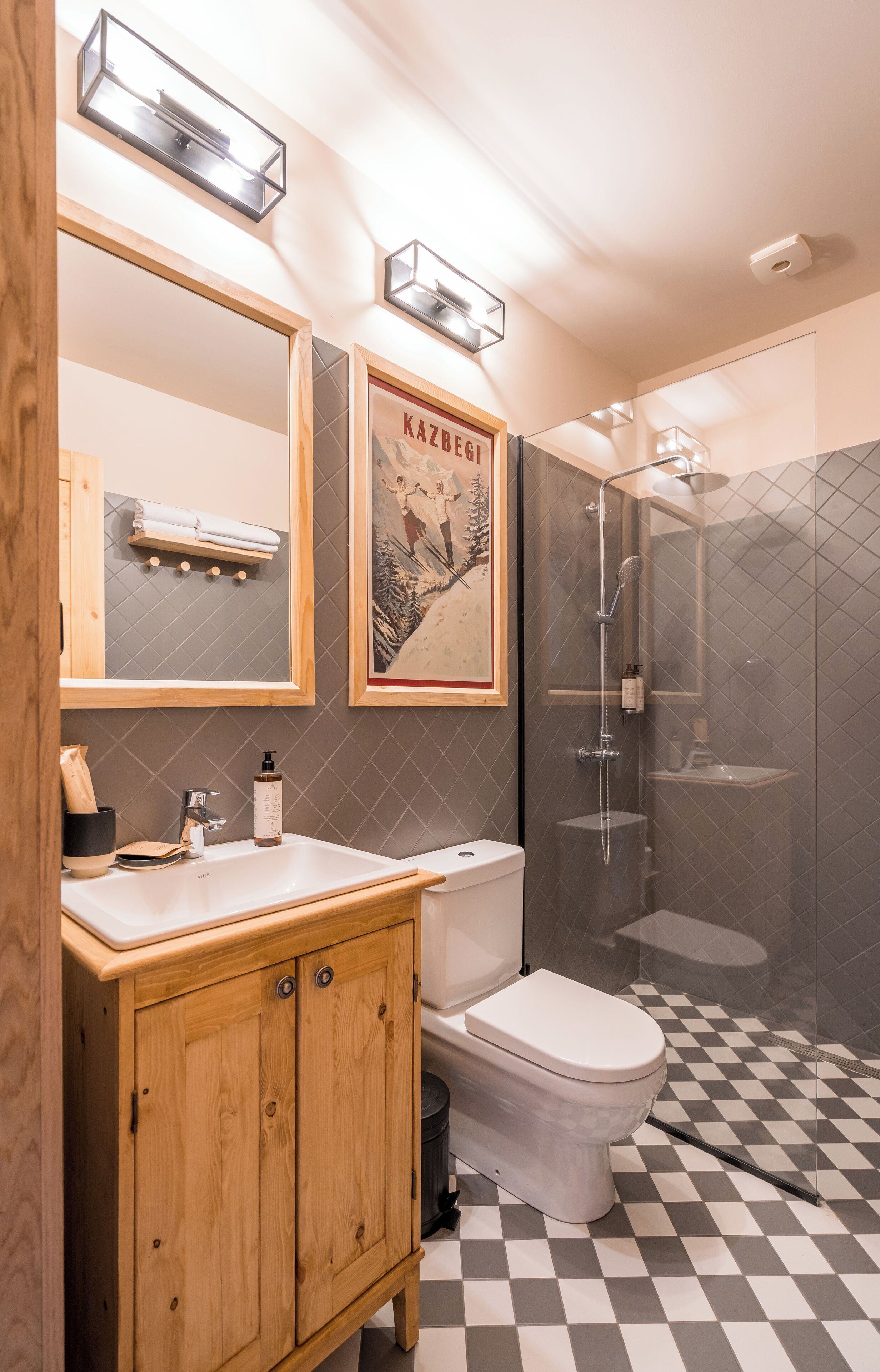 A modern bathroom with a wooden vanity, a white toilet, a glass-enclosed shower, and a checkered floor.