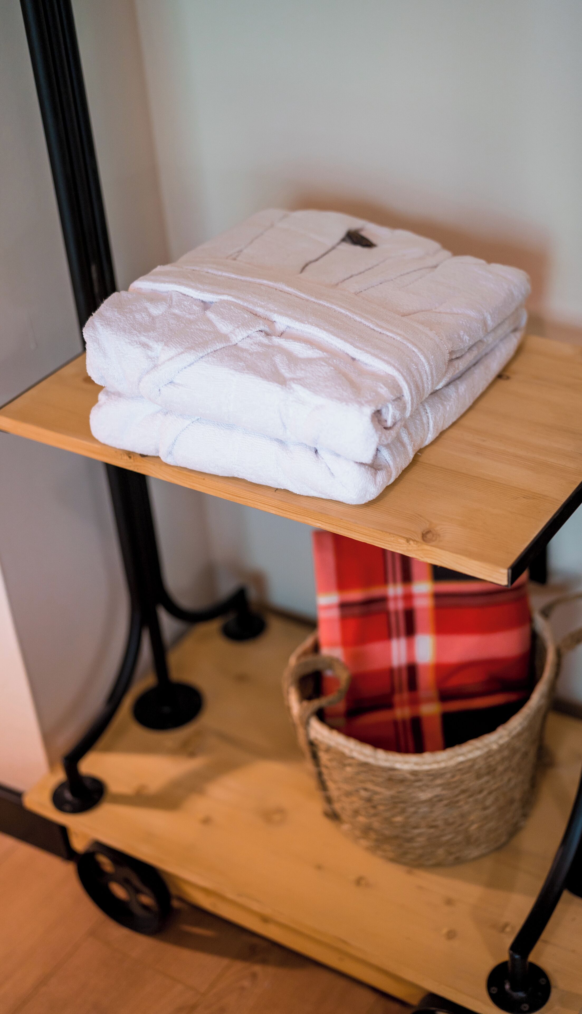 Une étagère en bois avec des serviettes blanches pliées et un panier en osier en dessous.