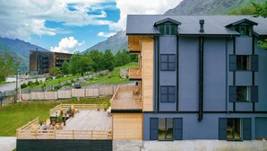 A modern multi-story building with a wooden deck, a balcony, and a view of mountains.