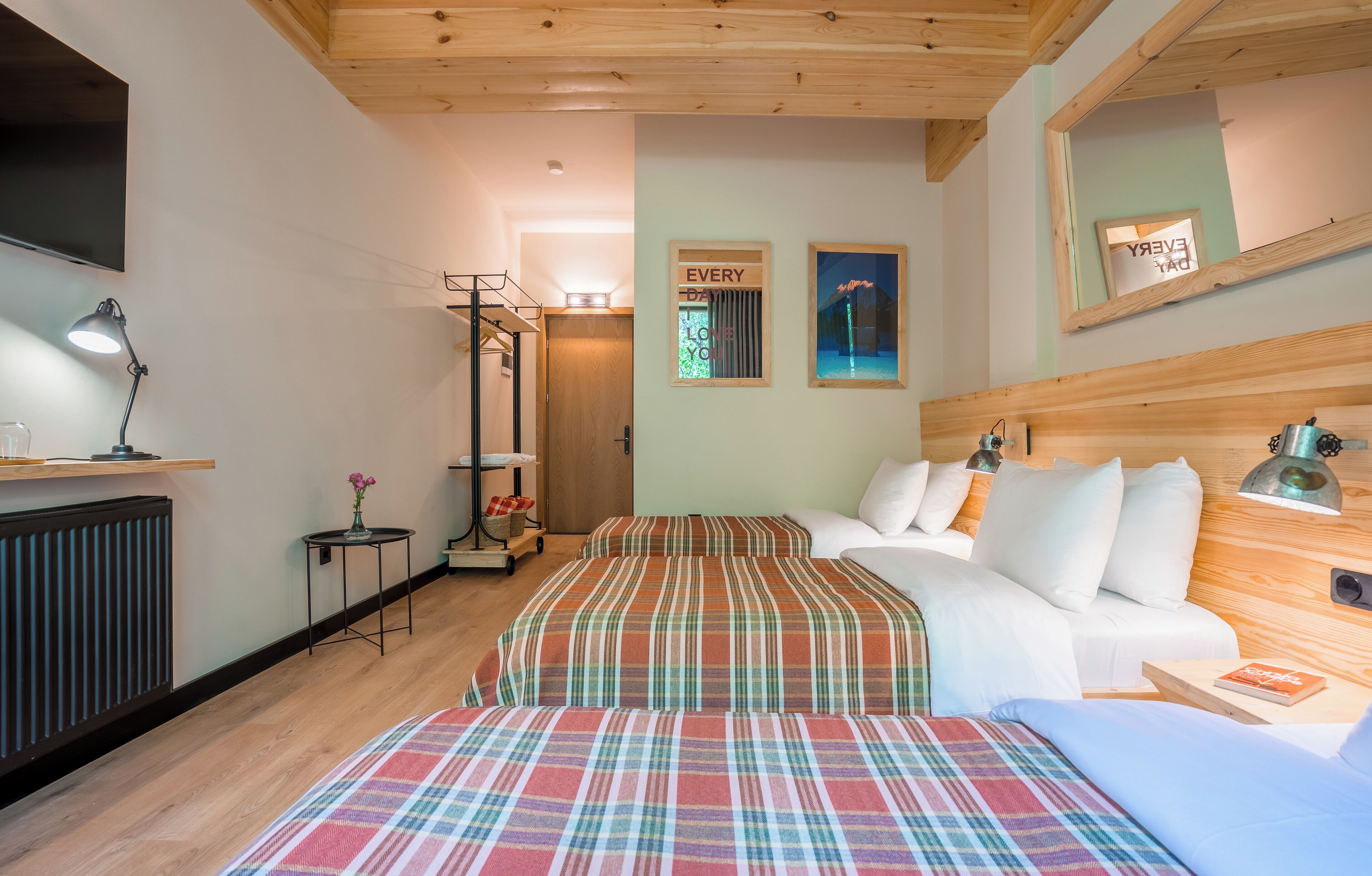 A hotel room with two beds, a sofa, a TV, a mirror, and a small table with a lamp.