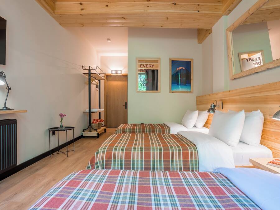 A hotel room with two beds, a sofa, a TV, a mirror, and a small table with a lamp.