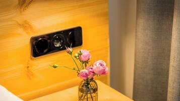 A wooden bedside table with a clear glass vase containing pink flowers, a metal lamp, and a power outlet.