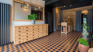 A modern hotel lobby with a checkered floor, a wooden console table with drawers, a large mirror, and a hanging light fixture.