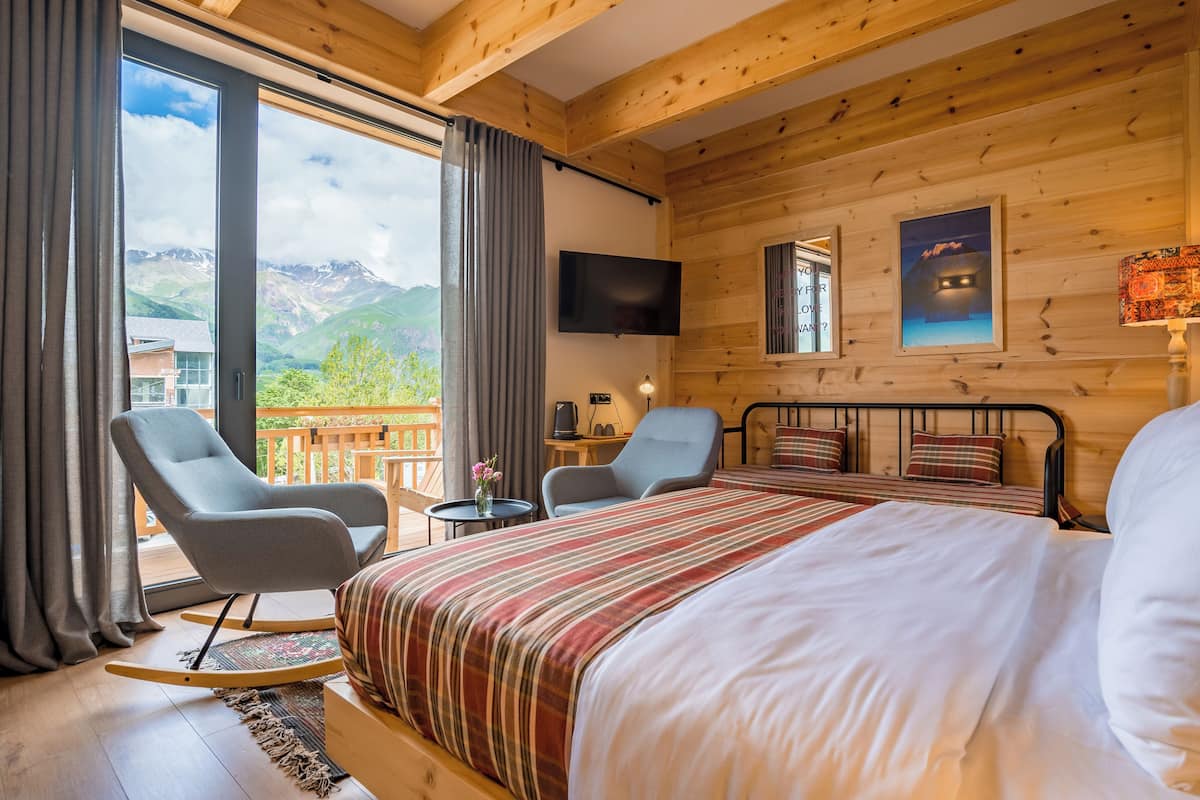 A wooden cabin room with a bed, two chairs, a table, and a TV.