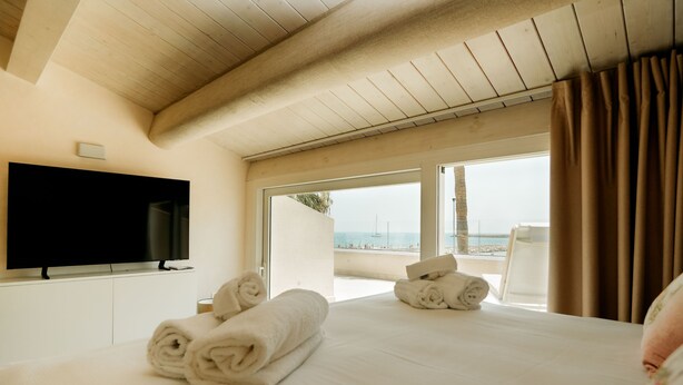 Ein Hotelzimmer mit einem großen Bett, einem Flachbildfernseher und Blick auf den Strand durch die Balkontüren.