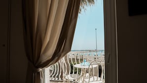 Ein Balkon mit weißen Metallstühlen und einem Tisch, Blick auf einen Strand und einen klaren Himmel.