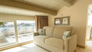Ein beiges Sofa mit zwei gemusterten Kissen, eine Schiebetür zu einem Sitzbereich im Freien und zwei gerahmte Bilder an der Wand.