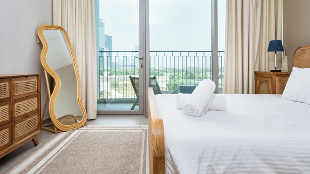 Habitación de hotel con cama, espejo, cómoda y balcón con vista a la ciudad.