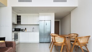 Una cocina moderna con armarios blancos, electrodomésticos de acero inoxidable y una zona de comedor con sillas y mesa de madera.