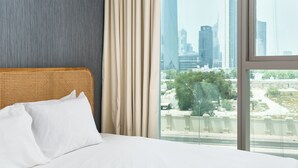 Habitación de hotel con un ventanal grande, una cama con ropa blanca y vistas a un horizonte urbano.