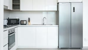 Una cocina moderna con armarios blancos, un refrigerador de acero inoxidable, un microondas, un tostador y un lavabo.