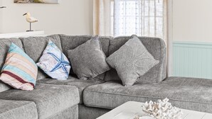 A living room with a grey sectional sofa, a white coffee table, and a window with sheer curtains. - Downtown OC Townhome! - (B) (Ocean City)