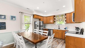 A kitchen with wooden cabinets, a refrigerator, a dishwasher, and a dining table with chairs. - Downtown OC Townhome! (A) (Ocean City)