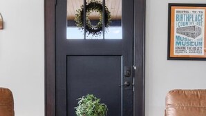 A dark wooden door with a wreath, a framed sign, two leather armchairs, a small round table with a plant and books, and a woven pouf. - Walk to State Street - Remodeled Home (Bristol)