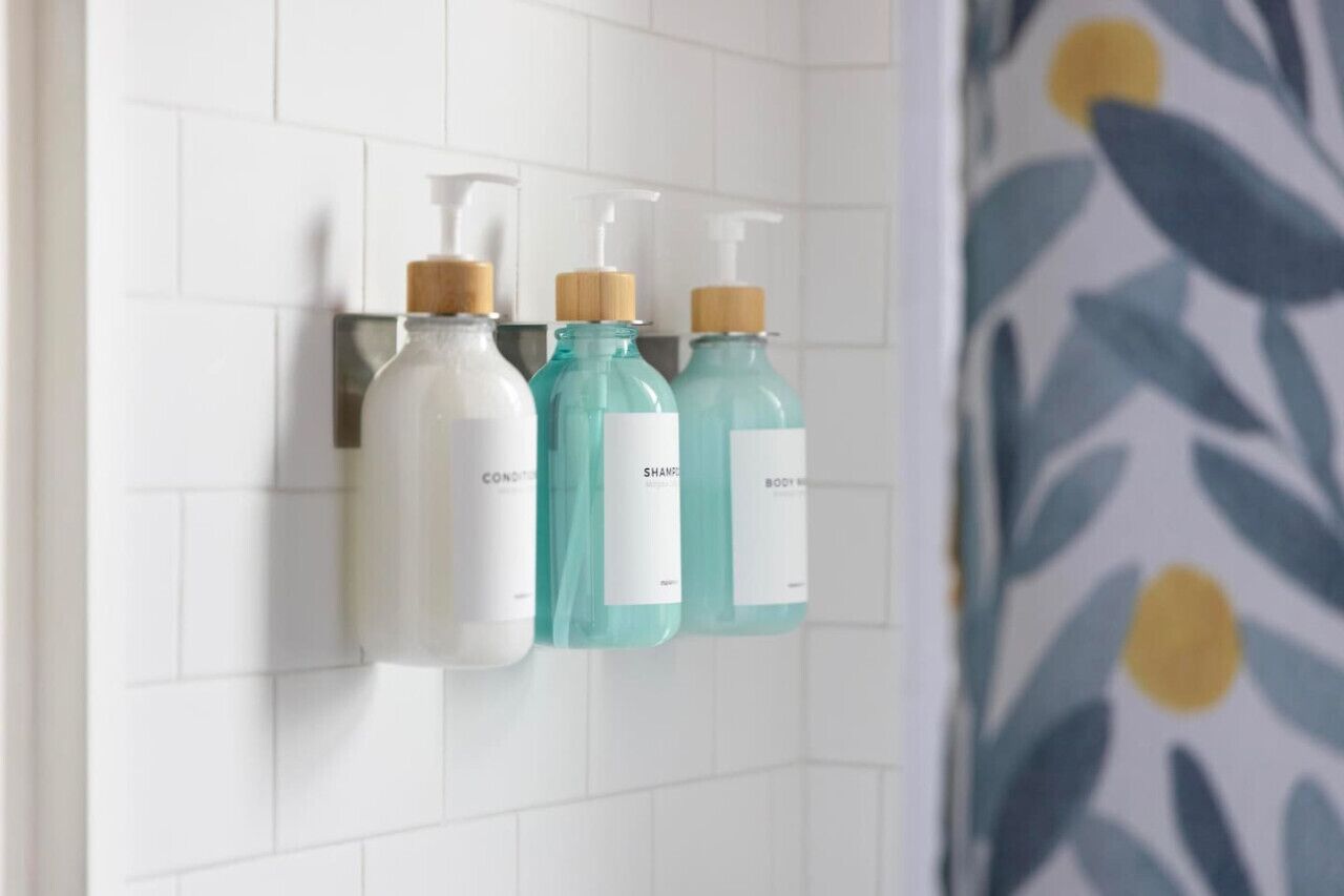 Three bottles of liquid soap on a white tiled wall.