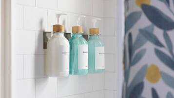 Three bottles of liquid soap on a white tiled wall.