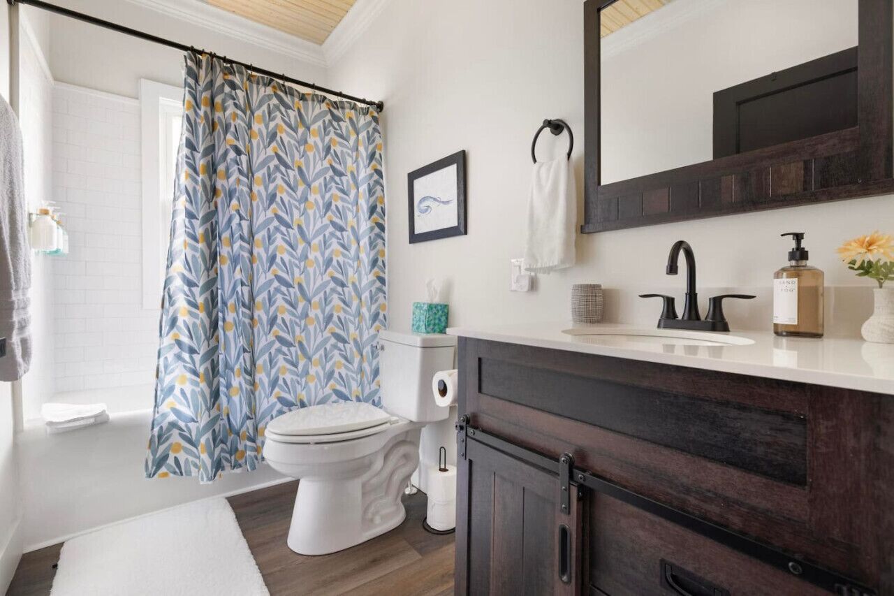 A bathroom with a shower curtain, toilet, sink, and dark wooden cabinets.