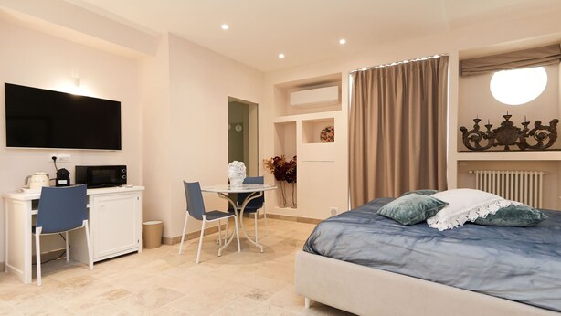 Ein Schlafzimmer mit einem Bett, einem Schreibtisch, einem Stuhl, einem Fernseher und einem kleinen Tisch mit einer Vase.