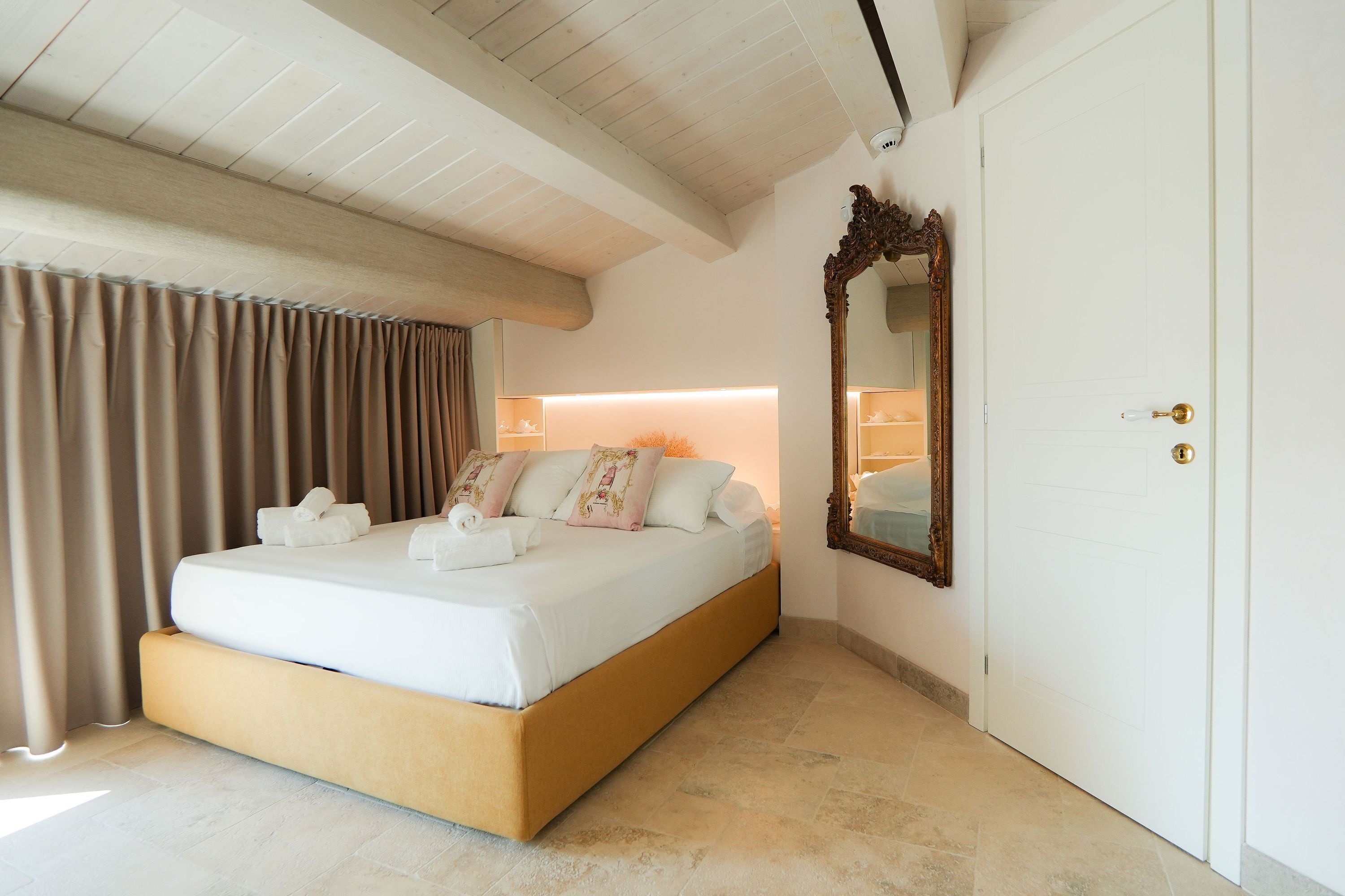 A bedroom with a bed, curtains, a mirror, and a door.