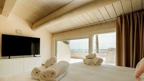 Une chambre d’hôtel avec un grand lit, un téléviseur à écran plat et une vue sur la plage depuis le balcon.