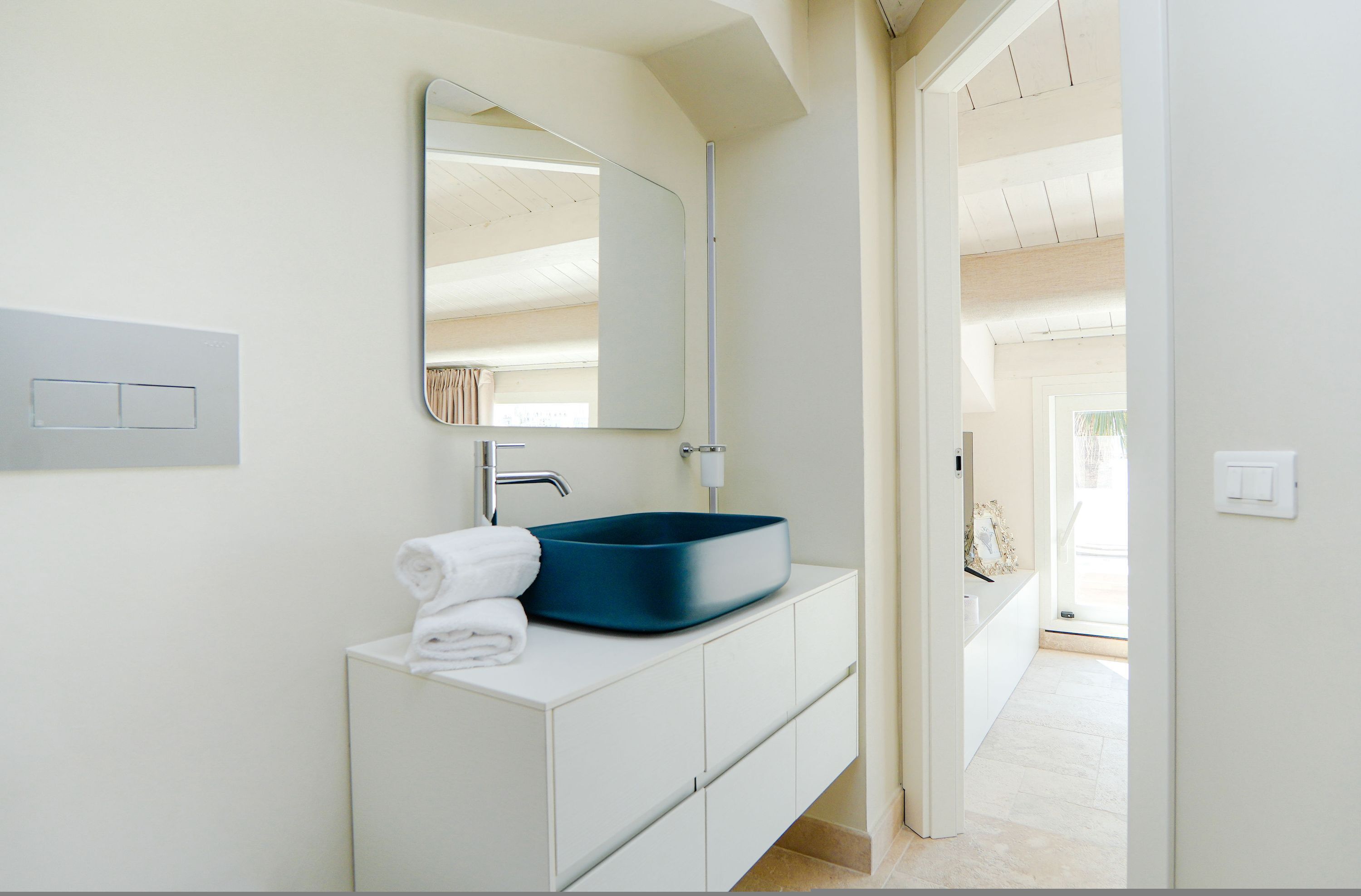 A modern bathroom with a white vanity, a blue basin, and a large mirror.