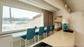 Une chambre d’hôtel moderne dotée d’une grande fenêtre, d’un coin repas avec des chaises, d’un lit et d’une lampe.